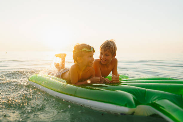 Photo of two boys laugh joyously as they splash and play in the ocean, creating lasting memories together under the bright sun.