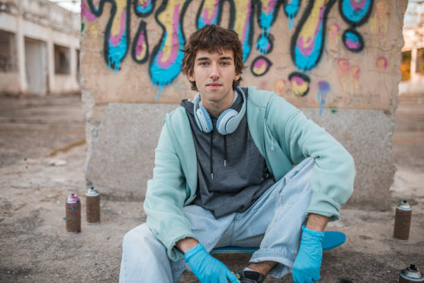 istock A young man looks directly into the camera while sitting in front of a graffiti he has drawn 2038108005