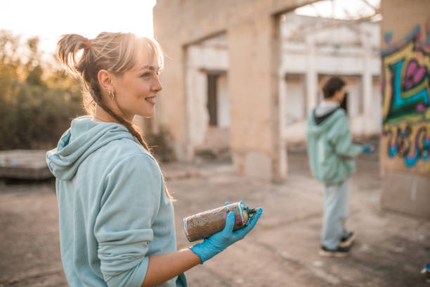 istock Cheerful woman holding spray paint in hands while drawing graffiti with friend 2038116145