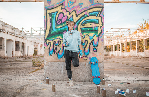 Street artist painting colored graffiti on public space wall - Modern art concept of urban guy performing and preparing live murales paint with yellow aerosol color spray - Cloudy afternoon filter