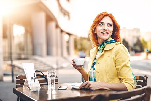 Smiling business woman is drinking coffee in a street cafe.