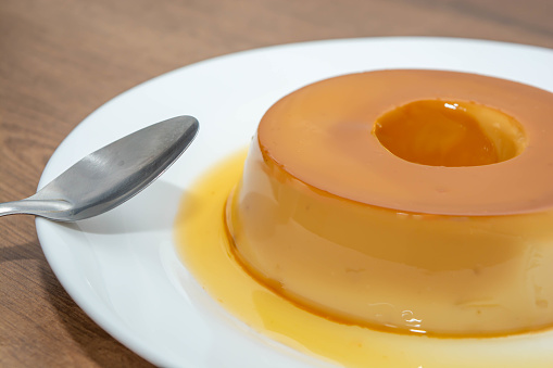 A pudim de leite, or pudding also known as flan on a wooden table with a metallic spoon