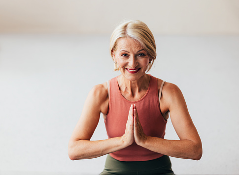 Active senior woman with blonde hair doing yoga, hands in prayer position, looking healthy and content.