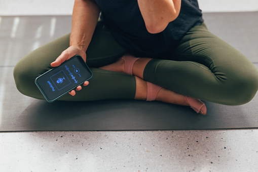 Close-up of a woman's hands holding a smartphone with fitness app during a yoga practice on a mat.