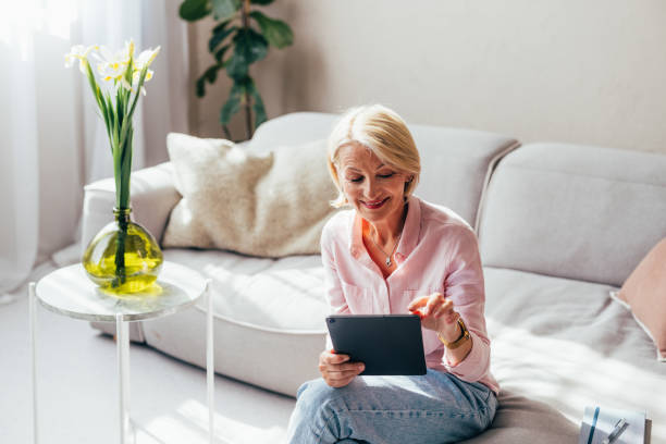 istock Smiling Senior Woman Using Tablet on Sofa at Home 2038150125