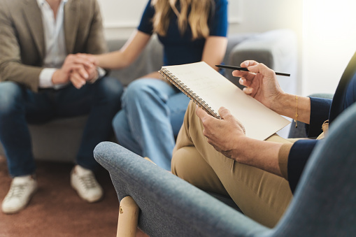 Couple therapy session: Therapist's notebook foregrounds while a young married couple holds hands in the background, seeking solutions to relationship challenges through counseling.