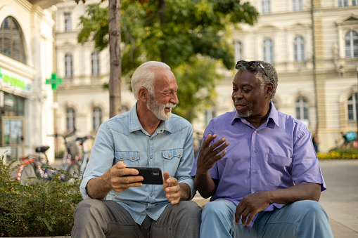 Two Diverse Senior Friends Having Fun With Mobile at City Street. Concepts About Elderly Lifestyle