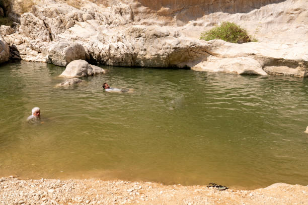 Two men swimming in a pond between rocks in oasis Wadi Bani Khalid.  Oman