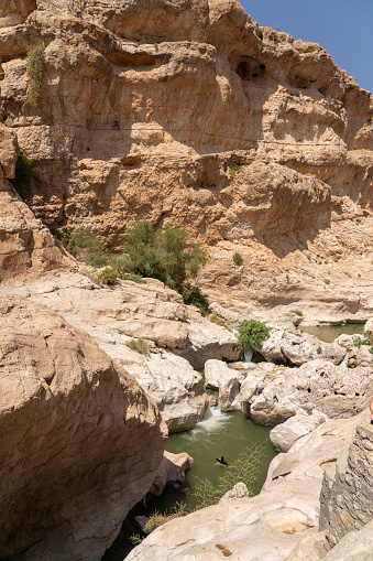 One person in rapids flowing among large rocks to swim in oasis Wadi Bani Khalid.  Oman