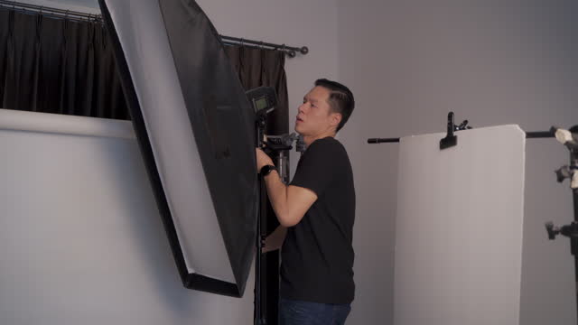 Asian photographer setting lighting and flash light and studio equipment in photography studio for taking pack shot product photo shoot. Home studio photographer.