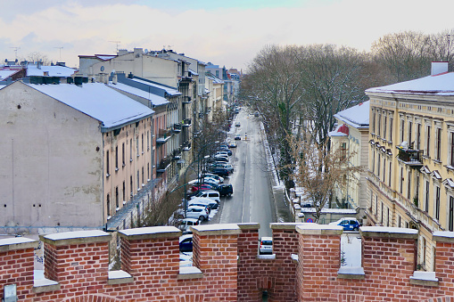 This long, straight Krakow street is bordered with pastel-colored building facades on the left and a public park on the right.