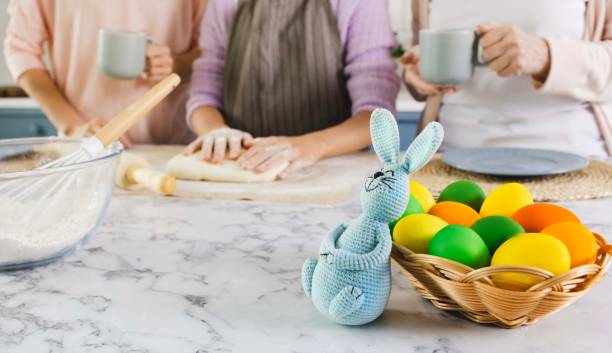 istock Basket with colorful eggs and Easter bunny on kitchen table during preparation to celebrate Easter holiday. Female part of family kneading dough for holiday pies and Easter bread 2038210192