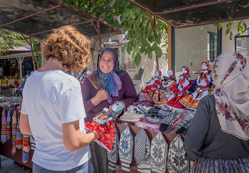 Soğanlı, Cappadocia, Turkey: a tourist buys a handmade rag doll dressed in typical cappadocian clothes from a turkish woman who bargains with her with a smile
