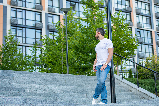 caucasian man in jeans outdoor. caucasian man in the street. caucasian man outside. photo of caucasian man in white shirt.