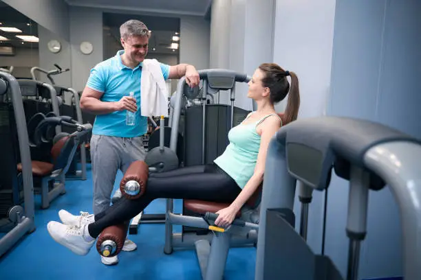 Smiling female exercising on leg extension machine while talking to pleased training companion