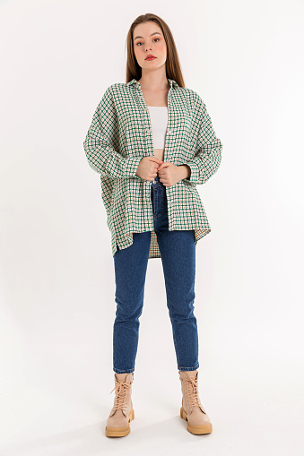 Brunette young woman wearing green white checkered shirt and blue jeans. Long sleeved shirt, comfortable jeans and brown boots.