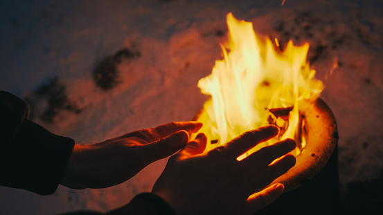 Detail of man warming hands by fire on frozen lake