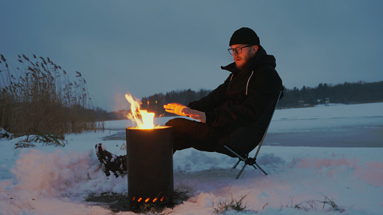 Man warms hands by fire on frozen lake