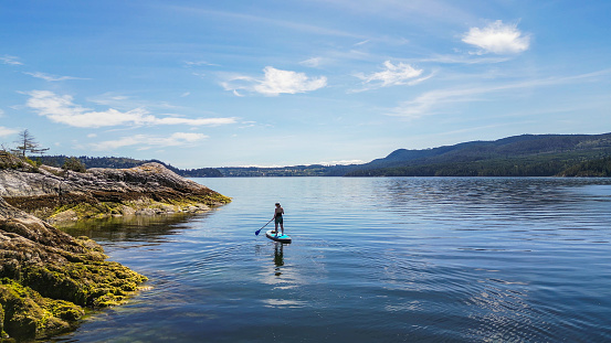 Aerial view of woman paddle boarding on ocean with mountains and forest