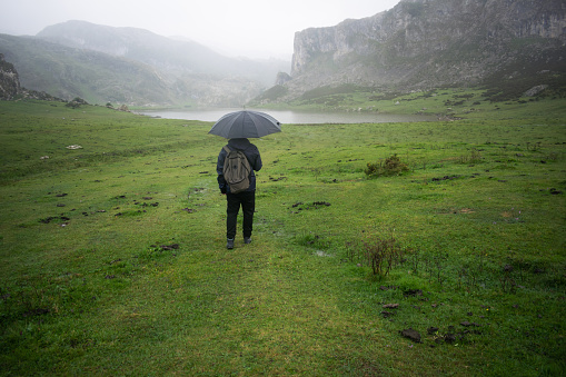 Back view of a man with raincoat and umbrella raining in Los Lagos de Covadonga