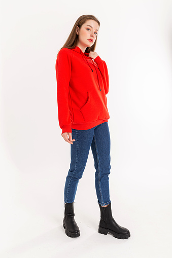 Brunette young woman wearing red hooded sweater, blue jeans. Long-sleeved,  wool sweatshirt, black boots.