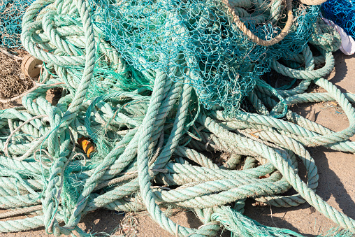 Close up shot of abandoned fishing net improperly disposed on a beach caused by the human fishing activity leading to fragmentation into microplastic contamination resulting in environmental problems.