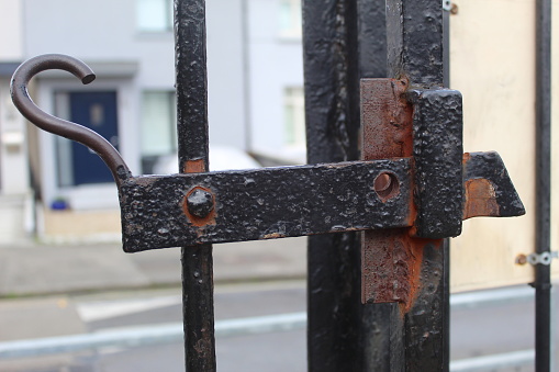 A close up photo of a black, antique and rusty gate lock beside a road.