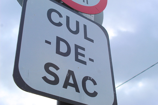 A photo of a white Irish Cul de sac road sign against a cloudy sky.