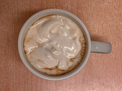 Cup of coffee with foam on wooden table. Top view.