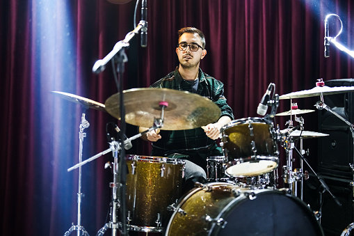 A male drummer plays snare drum with drumsticks in a dark room.