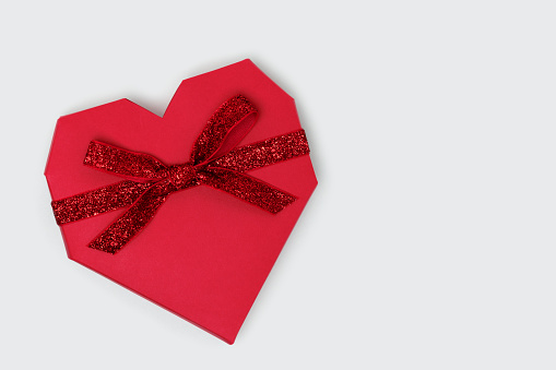 Red gift box in a heart shape with tied glittering ribbon on a blue background.