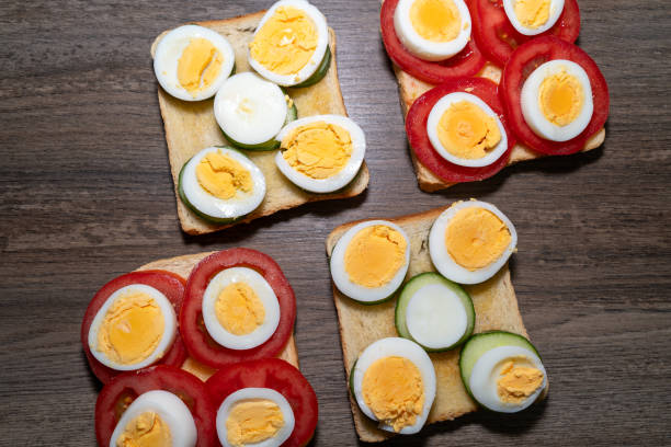 Toasted bread with boiled eggs, tomatoes and cucumber slices on the wooden kitchen counter