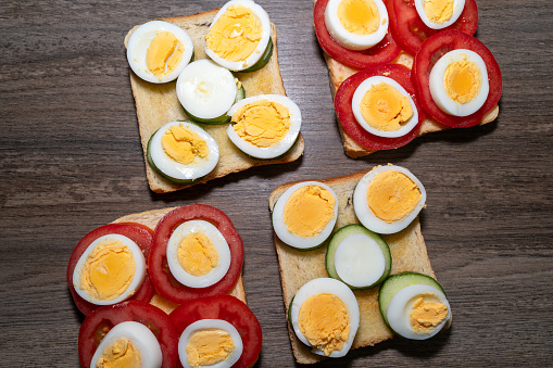 Toasted bread with boiled eggs, tomatoes and cucumber slices on the wooden kitchen counter