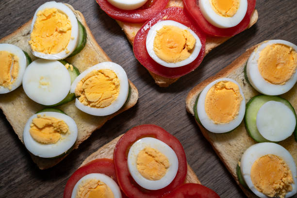 Toasted bread with boiled eggs, tomatoes and cucumber slices on the wooden kitchen counter