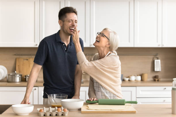 Joyful older mom and son baking together, cooking breakfast