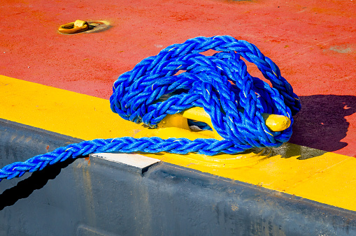 Close-up of a sailor's hands, firm and experienced, as they grip the thick, coiled ropes aboard a ship. Each strand of the rope tells a story of the sea, a symbol of the strength and resilience required to navigate the waters. The sailor's grey dress, accented with a black embroidered belt, hints at a blend of functionality and formality, while beaded bracelets add a touch of personal style to the seafaring attire.