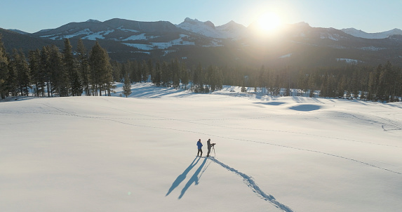 Aerial view of mature couple taking photos in snowy winter landscape with snowcapped mountains distant