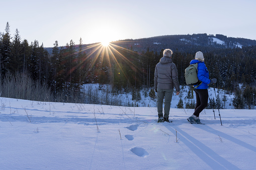 Mature couple hike watch sunrise over mountains in winter with snowcapped mountains distant