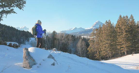 Mature woman hikes in snowy winter landscape with snowcapped mountains distant, Crowsnest Peak