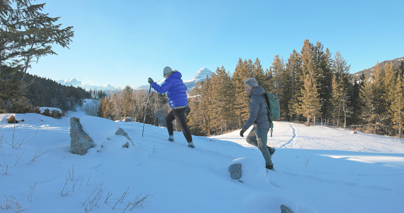 Mature couple hike in snowy winter landscape with snowcapped mountains distant, Crowsnest Peak