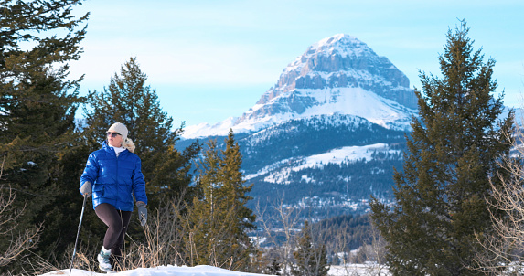 Mature woman hikes in snowy winter landscape with snowcapped mountains distant, Crowsnest Peak