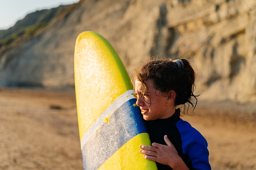 Teenage girl holding surfboard and looking at the waves