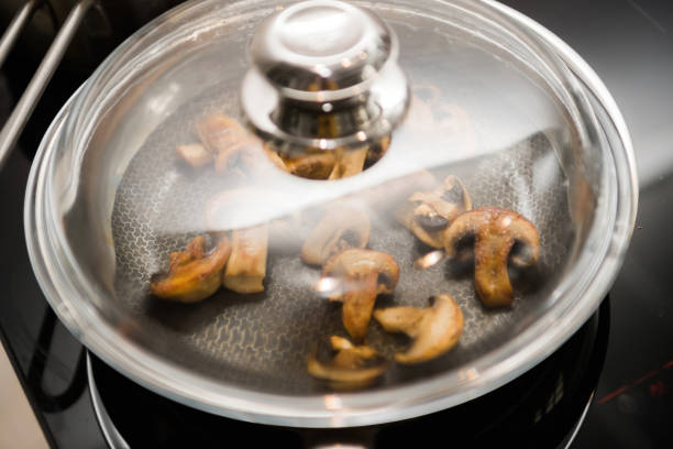 Close-up defocused view of an with frying mushroom inside covered with glass lid