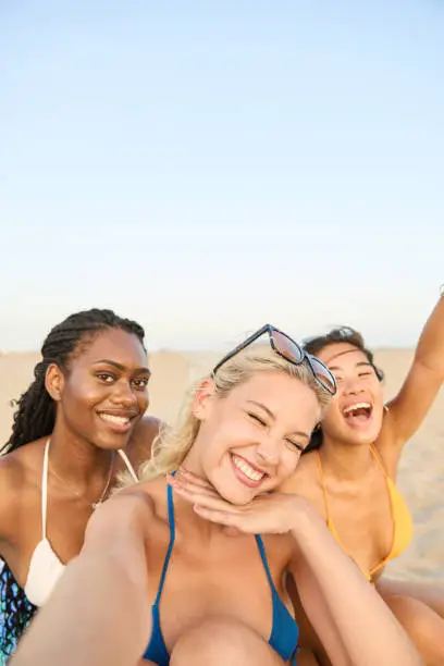 Cheerful group of young multiethnic friends in bikinis take a selfie with their mobile phone while enjoying a summer day on the beach during their holidays. Cheerful group of young multiethnic friends in bikinis take a selfie with their mobile phone while enjoying a summer day on the beach during their holidays.