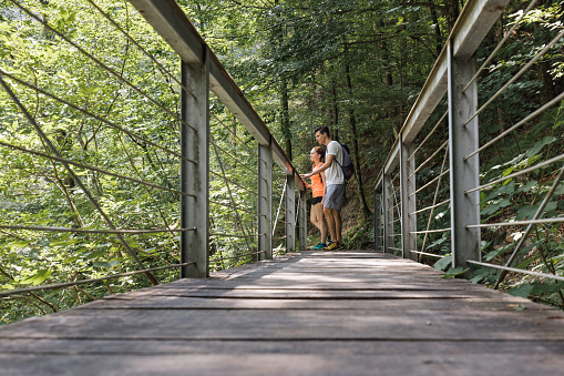 Loving couple, recreational hikers, crossing a suspension bridge over a rocky mountain river bed. Adventure and travel concept.