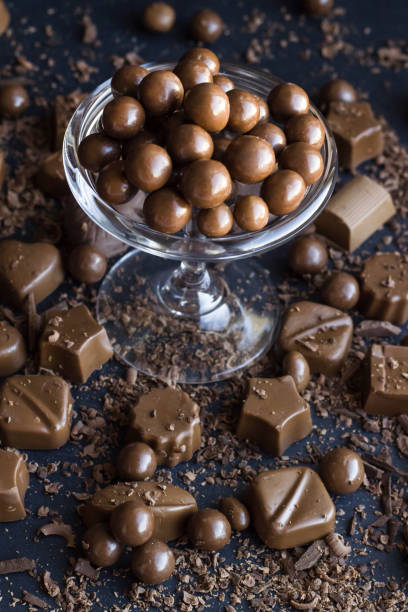 palla di nocciole ricoperte di cioccolato con gocce di cioccolato grattugiato in un'elegante ciotola, su superficie nera - scoop in front of portion colors foto e immagini stock