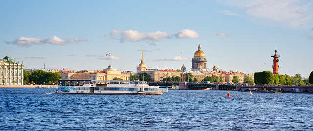 Cityscape of old history buildings on embankment Neva river, Saint Isaac's Cathedral and Spit of Vasilievsky Island, Saint-Petersburg, Russia. Tourist boat in the foreground. Blue cloudy sky.