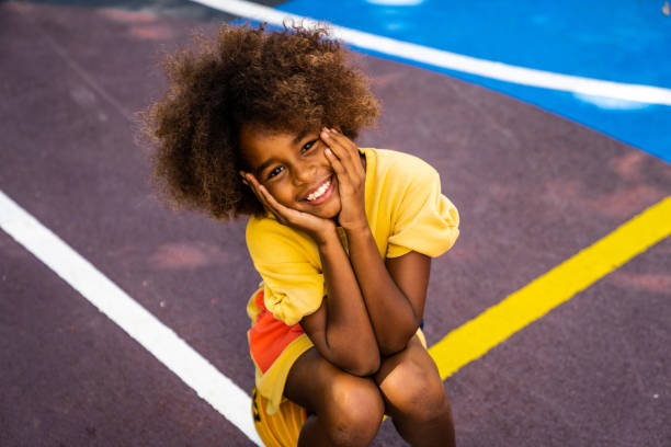 A young beautiful girl is smiling while sitting on the basketball court.
