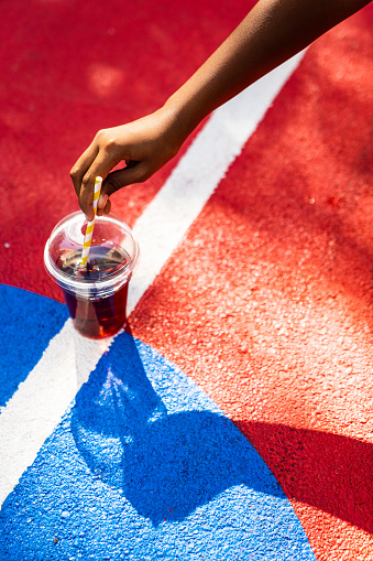 A cup of juice with the lid and a straw is on the outdoor basketball court.