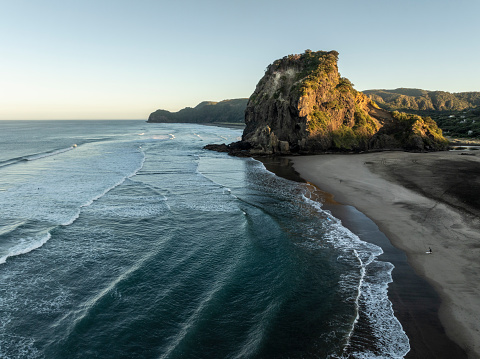 Piha/s iconic Lion Rock shot from the air on a crisp clear morning with fun surf rolling in.